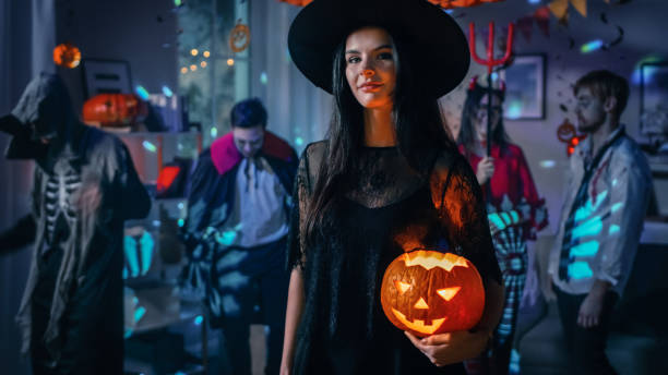 fête de costume d’halloween: magnifique sorcière séduisante portant robe tient brûlant citrouille. contexte: beau diable, mort effrayante, comte dracula, zombie dansant dans la salle décorée - witches & vampires photos photos et images de collection