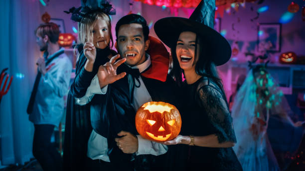 halloween costume party: père comte dracula détient petite chauve-souris fille fille et câlins sorcière femme pour un portrait de famille heureux. dans les monstres de fond s’amuser - witches & vampires photos photos et images de collection