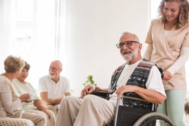 istock Senior man on wheelchair with helpful caregiver supporting him 1155615967