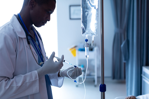 Médico masculino inyectando inyección a pacientes hembra goteo intravenoso en el pabellón photo