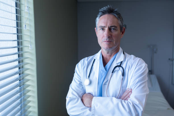 medico maschio maturo in piedi con le braccia incrociate in ospedale - doctor male doctor mature men portrait foto e immagini stock