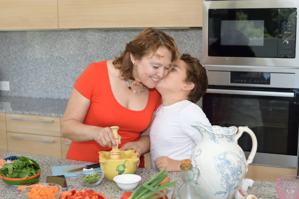 сын целует свою мать, пока они готовят обед - family with one child domestic life caucasian love стоковые фото и изображения