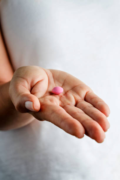 istock Single pink pill on young woman hands 1155628095