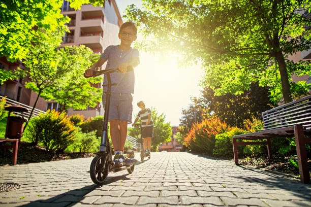 les enfants surfant des scooters dans la zone résidentielle de ville. - family outdoors cheerful nature photos et images de collection