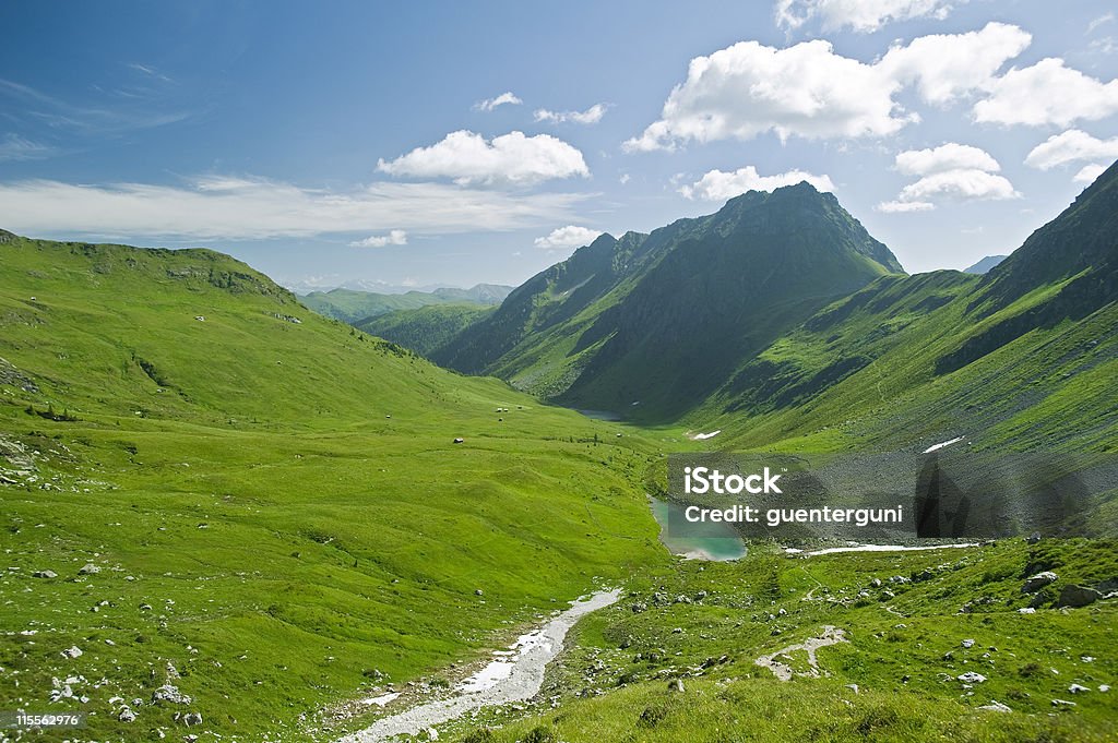 Alpine vale with mountains surrounding Panoramic view of  a green alpine meadow,  a small alpine lake and the summits of the Carnic Alps in Austria.  Austria Stock Photo