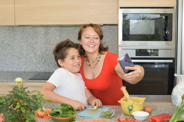 matriz e filho felizes que preparam o almoço quando tomam um ' selfie ' - family with one child domestic life caucasian love - fotografias e filmes do acervo