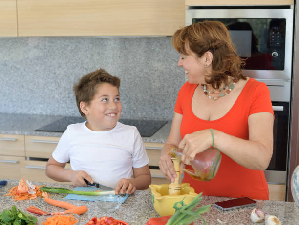 matriz e filho que preparam o almoço e o sorriso. o filho corta o alho - family with one child domestic life caucasian love - fotografias e filmes do acervo