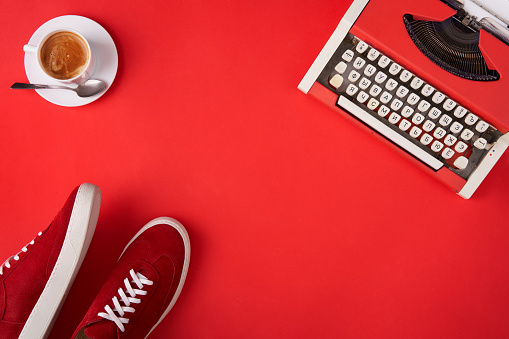Bright red shoes, typewriter and coffee cup on red background, top view style. Inspiration concept