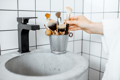 A bucket with makeup brushes on the modern sink in the bathroom