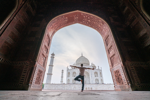 Young man practicing yoga in India at the famous Taj Mahal at sunrise - People travel spirituality zen like concept