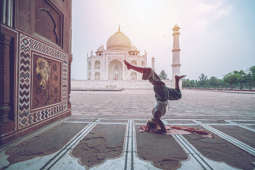 Young woman practicing yoga in India at the famous Taj Mahal at sunrise - Headstand position upside down- People travel spirituality zen like concept