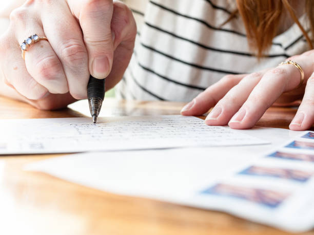 woman writing on a postcard - writing letter correspondence women imagens e fotografias de stock