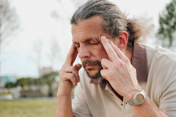 istock A tired and distressed aged man sits on a park bench. Leans on his hands, rubs his temples. 1155676417