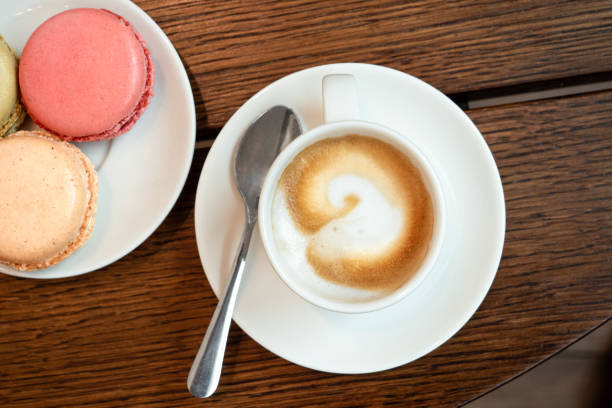 istock Espresso macchiato in white ceramic cup with saucer and spon next to a plate with macarons on brown wood surface from above. 1155676909