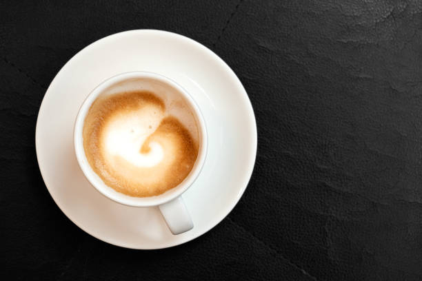istock Espresso macchiato in white ceramic cup with saucer isolated on black leather surface from above. Space for text. 1155676928