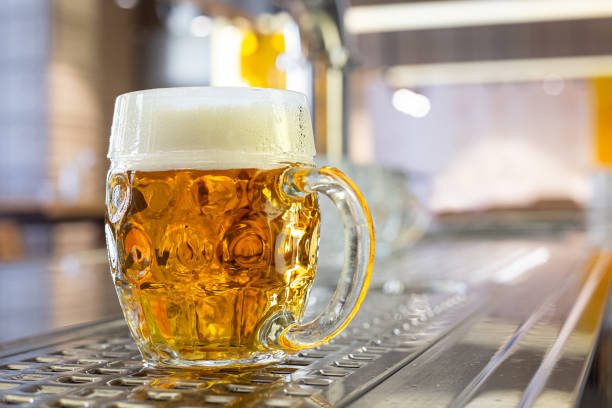 freshly poured draft lager beer in a dimpled glass mug on stainless steel counter in a modern pub. space for text. - dimple imagens e fotografias de stock