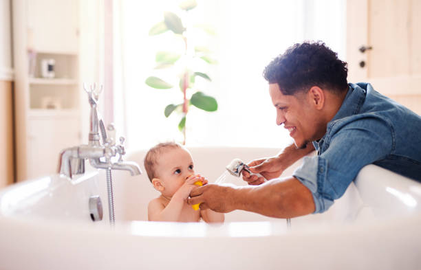 Father washing small toddler son in a bathroom indoors at home. Hispanic father washing small toddler son in a bathroom indoors at home. bathtub stock pictures, royalty-free photos & images
