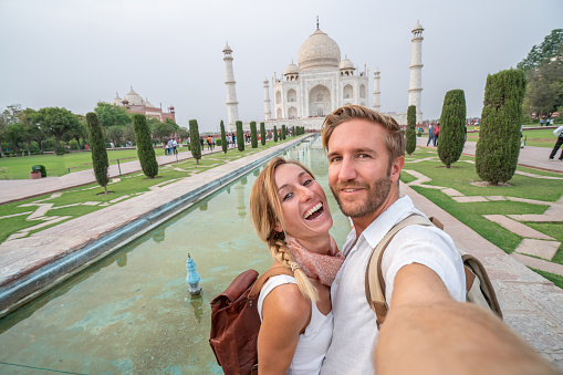 Young couple taking selfie portrait at the Taj Mahal international landmark in India - People travel the world concept