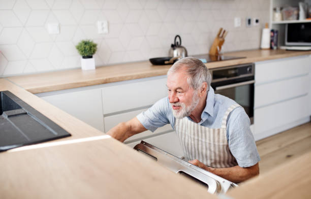 istock A senior man indoors in kitchen at home, loading dishwasher. 1155681541