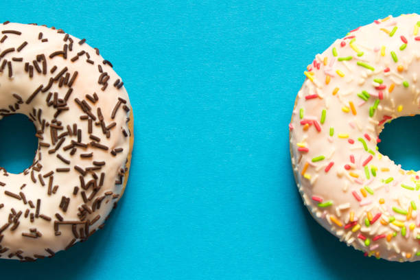 istock Fresh glazed donuts with chocolate and colorful sprinkles on a orange background. 1155687030