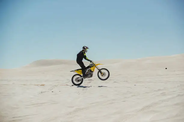 Motorcyclist riding his bike across sand dunes.