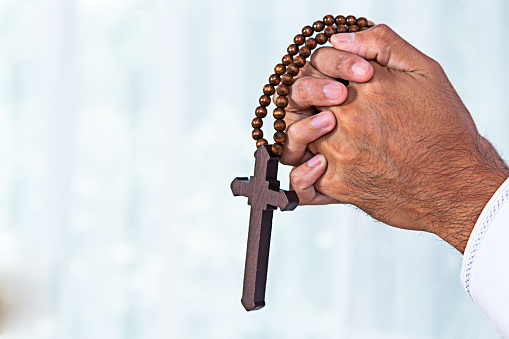 old female hands praying and holding a rosary