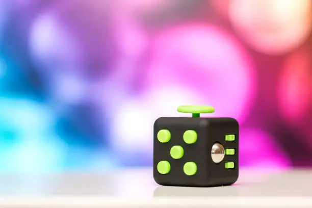 Photo of Fidget cube anti stress toy. Detail of finger play toy used for relax. Gadget placed on colorful bokeh background