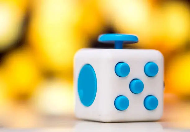 Photo of Fidget cube anti stress toy. Detail of finger play toy used for relax. Gadget placed on colorful bokeh background