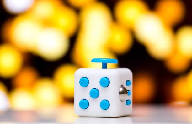 Photo of Fidget cube anti stress toy. Detail of finger play toy used for relax. Gadget placed on colorful bokeh background