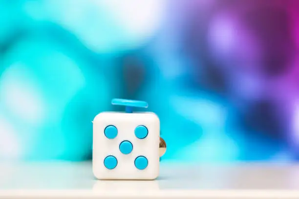 Photo of Fidget cube anti stress toy. Detail of finger play toy used for relax. Gadget placed on colorful bokeh background