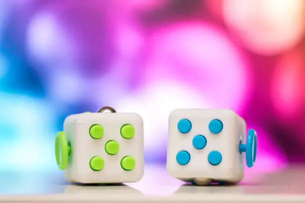 Photo of Fidget cube anti stress toy. Detail of finger play toy used for relax. Gadget placed on colorful bokeh background