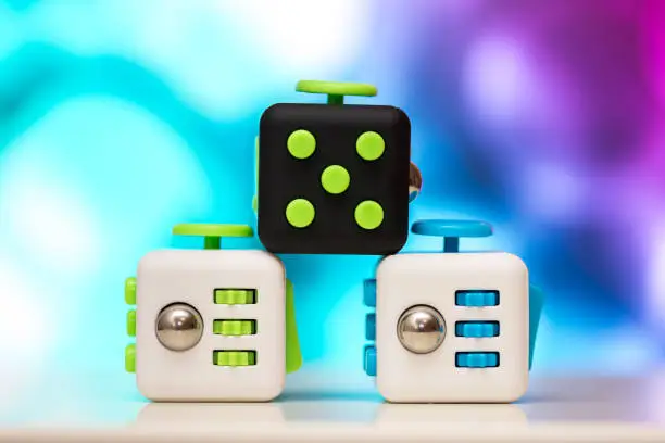 Photo of Fidget cube anti stress toy. Detail of finger play toy used for relax. Gadget placed on colorful bokeh background