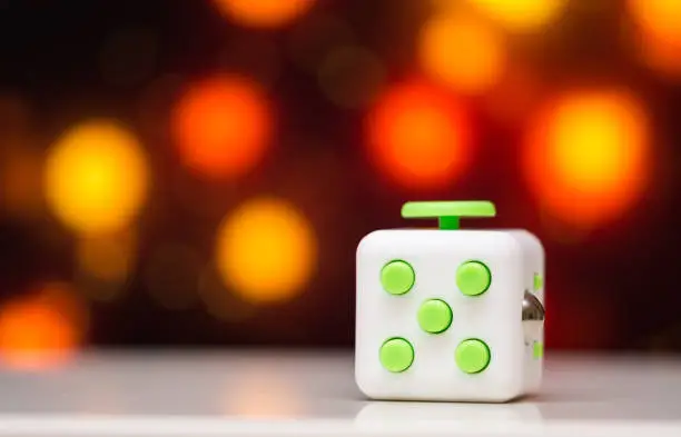 Photo of Fidget cube anti stress toy. Detail of finger play toy used for relax. Gadget placed on colorful bokeh background