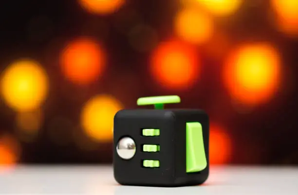 Photo of Fidget cube anti stress toy. Detail of finger play toy used for relax. Gadget placed on colorful bokeh background