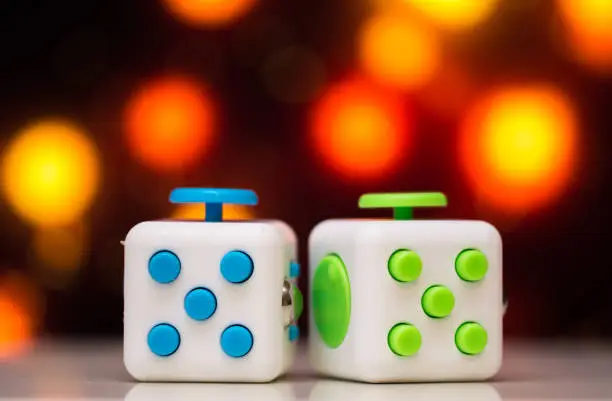 Photo of Fidget cube anti stress toy. Detail of finger play toy used for relax. Gadget placed on colorful bokeh background