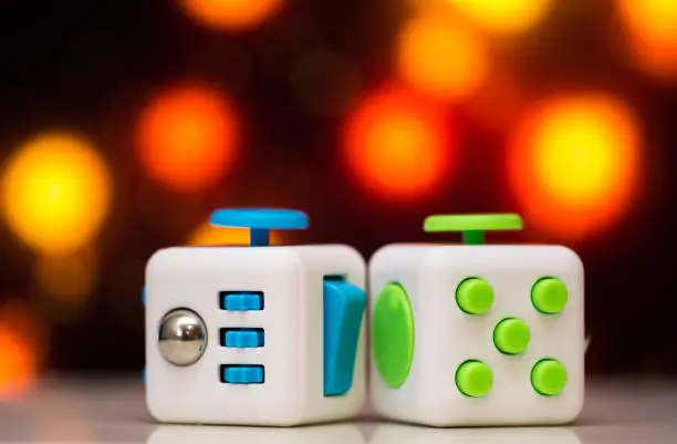 Photo of Fidget cube anti stress toy. Detail of finger play toy used for relax. Gadget placed on colorful bokeh background