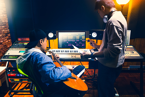 male asian producer consulting with professional guitarist about style of a song to record in recording studio