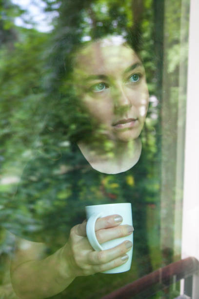 istock Young woman looking out window view through glass 1155700765