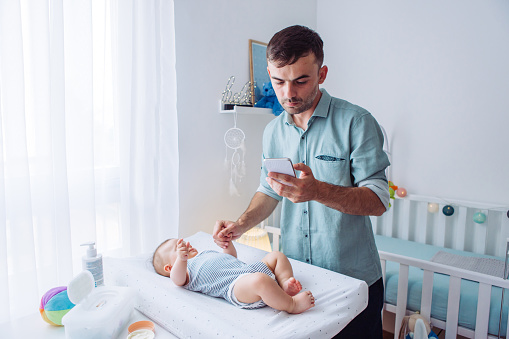 Father and baby boy in baby room, father calling pediatrician with phone for advice