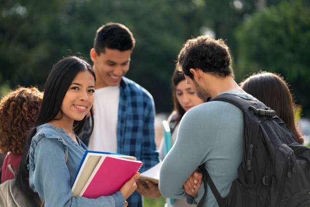istock Latin american college students talking as a group while female student faces camera smiling 1155707622