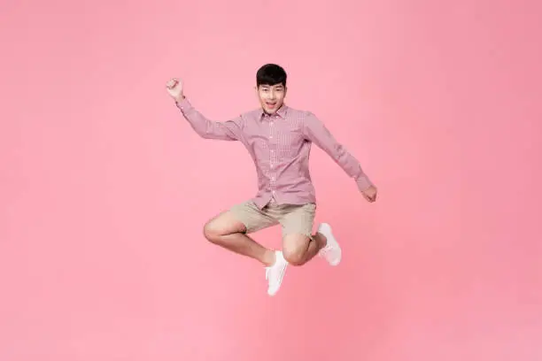 Photo of Energetic smiling young Asian man in casual clothes jumping