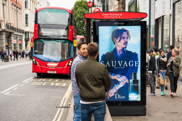 London: Oxford Street bus stop London, UK - People on an Oxford Street pavement near a bus stop, as a double-decker bus arrives. The JCDecaux digital display on the bus stop features Johnny Depp in an advertisement for Sauvage by Dior. photo fame stock pictures, royalty-free photos & images