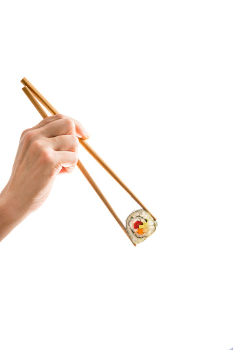 Young female hand holding wooden chopsticks with a freshly prepared vegan maki sushi roll - backlit, cutout isolated on white background, copy space