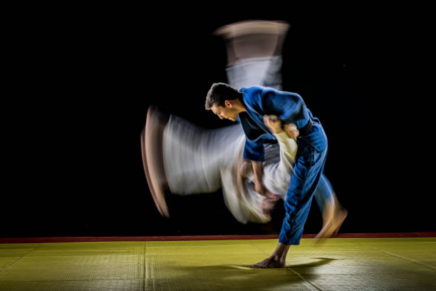 Blurred judo throw Blurred motion photo of a male judo practitioner in a blue kimono throwing his partner in a white kimono to the ground. Black background. judo photos stock pictures, royalty-free photos & images