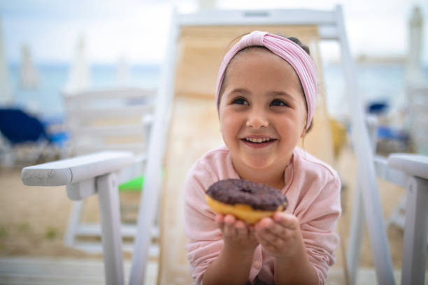 la bambina carina tiene con impazienza una ciambella - focus on foreground joy happiness pink foto e immagini stock