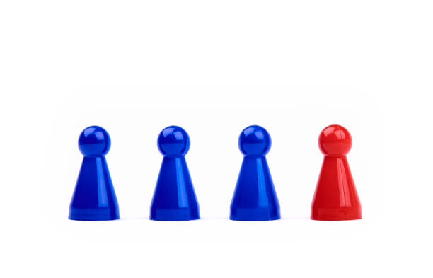 drei blaue spielsteine und eine rote figur, die neben ihnen als anführer, boss oder anders steht. verschwommener schwarz-weißer hintergrund. - chess pawn red blue leisure games stock-fotos und bilder
