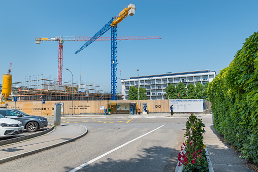 Mendrisio, Switzerland  – June 4, 2019: Mendrisio Regional Hospital (OBV), new wing construction work (as written on white billboard). Work on widening the civil hospital called Beata Vergine. This hospital is part of the EOC (Ente Ospedaliero Cantonale - cantonal hospital organization). Mendrisio is a municipality in the district of Mendrisio in the canton of Ticino in southern Switzerland,
