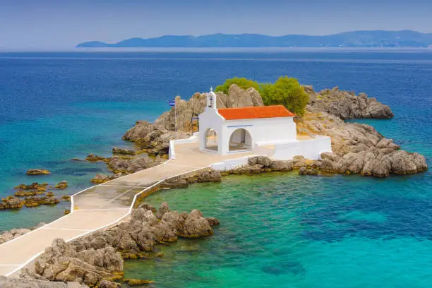 A classical white greek church on a small rocky island in Agios Isidoros, Greece