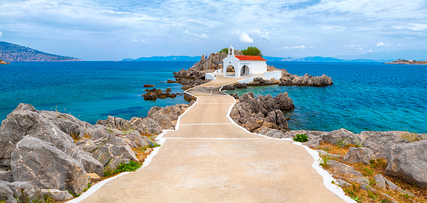 A classical white greek church on a small rocky island in Agios Isidoros, Greece