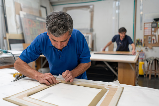 Portrait of an adult Latin American man working at carpentry making a picture frame